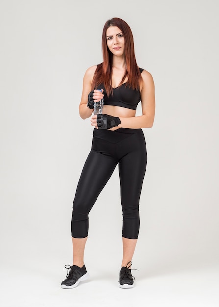 Vista frontal da mulher atlética em trajes de ginástica, segurando a garrafa de água