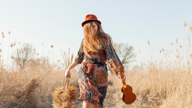 Vista frontal da mulher boêmia na natureza segurando o ukulele