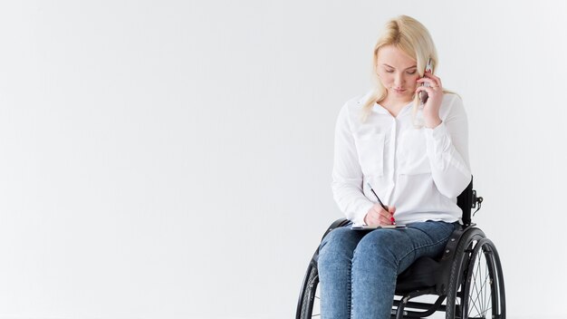 Vista frontal da mulher em cadeira de rodas, trabalhando e falando ao telefone