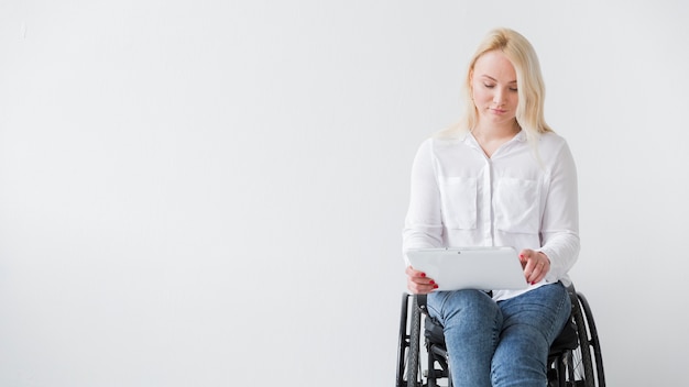 Vista frontal da mulher em cadeira de rodas, trabalhando em tablet