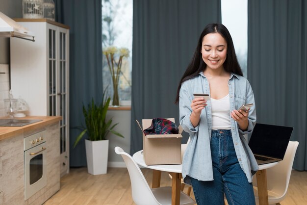 Vista frontal da mulher fazer pedidos on-line enquanto olha para o cartão de crédito