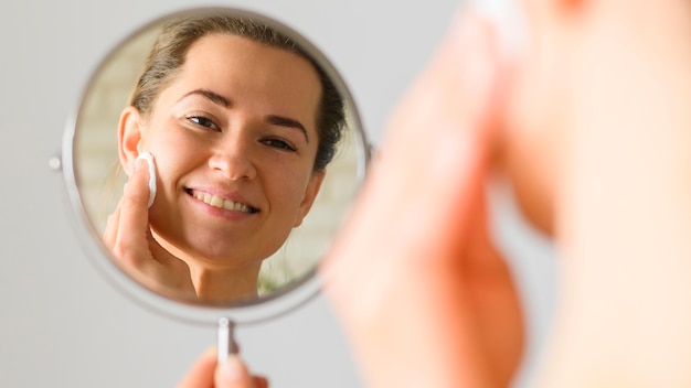 Vista frontal da mulher limpando o rosto no espelho
