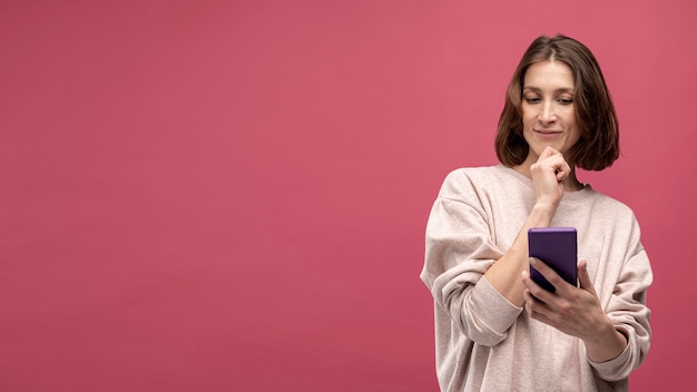 Vista frontal da mulher pensando enquanto segura o smartphone