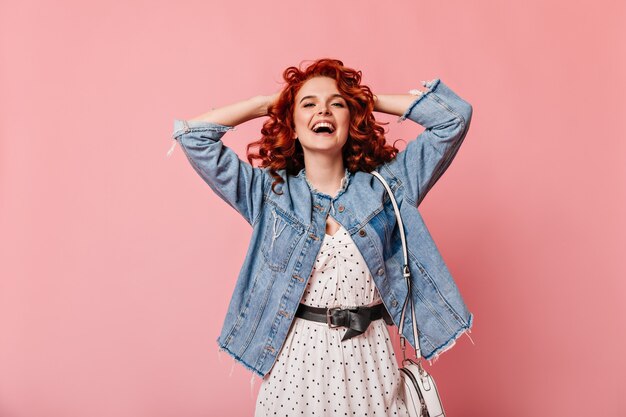 Vista frontal da mulher romântica rindo sobre fundo rosa. Foto de estúdio de menina bem-humorada em jaqueta jeans casual.