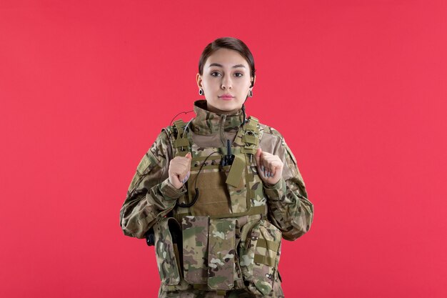 Vista frontal da mulher soldado em uniforme militar na parede vermelha