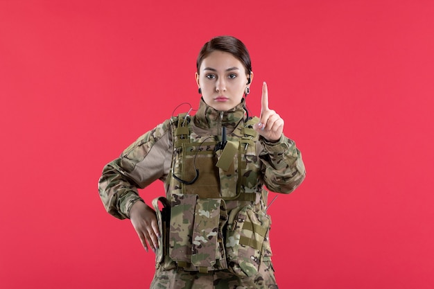 Vista frontal da mulher soldado em uniforme militar na parede vermelha