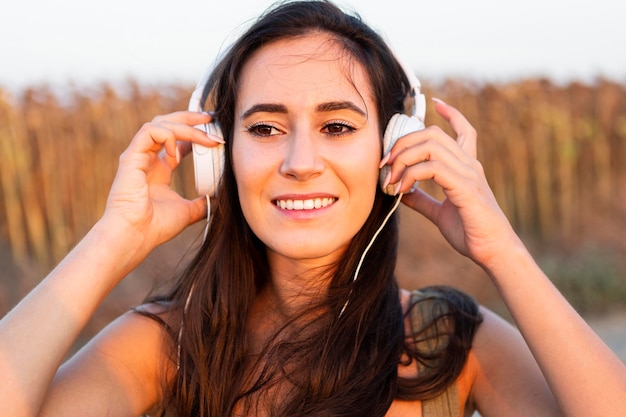 Foto grátis vista frontal da mulher sorridente com fones de ouvido no pôr do sol