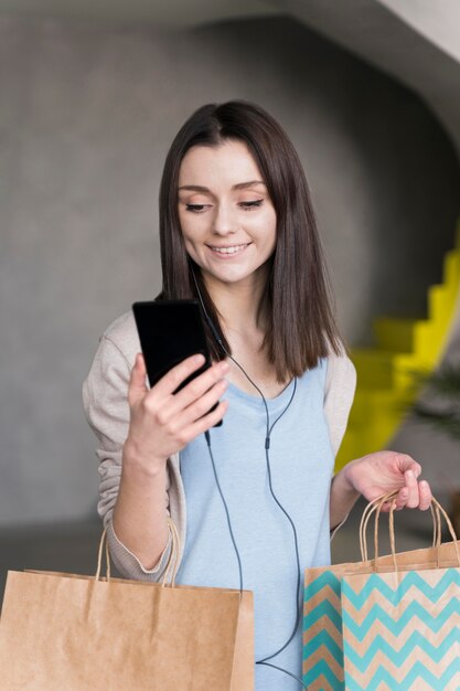 Vista frontal da mulher sorridente segurando sacos de papel e smartphone