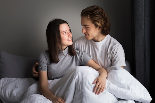 Vista frontal da mulher sorrindo para o namorado enquanto está sentado na cama