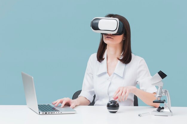 Vista frontal da mulher usando laptop e fone de ouvido de realidade virtual