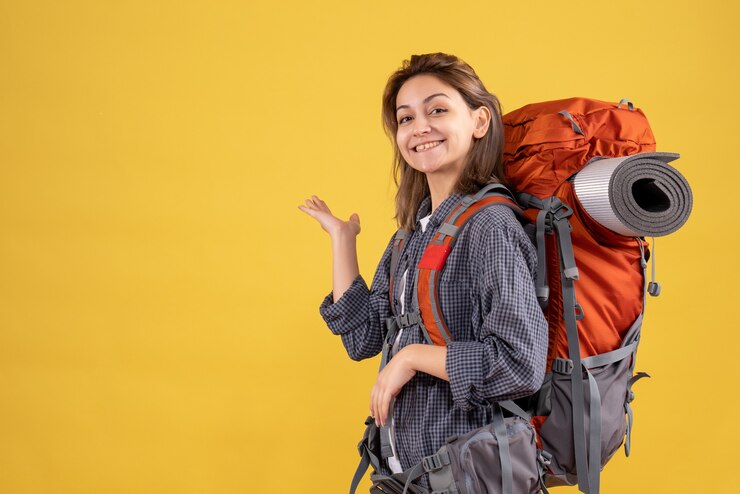 Foto grátis vista frontal da mulher viajante feliz com mochila vermelha apontando para a parede