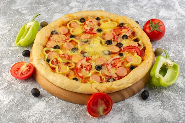 Vista frontal da pizza de queijo com azeitonas, salsichas e tomates vermelhos na mesa cinza