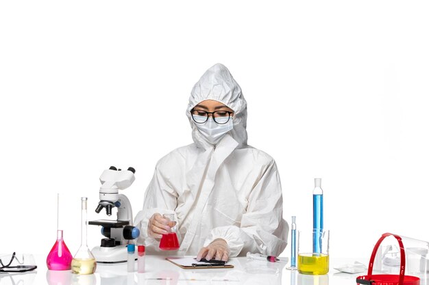 Vista frontal da química feminina em traje de proteção especial segurando uma solução vermelha no laboratório de vírus covid-química de fundo branco-claro