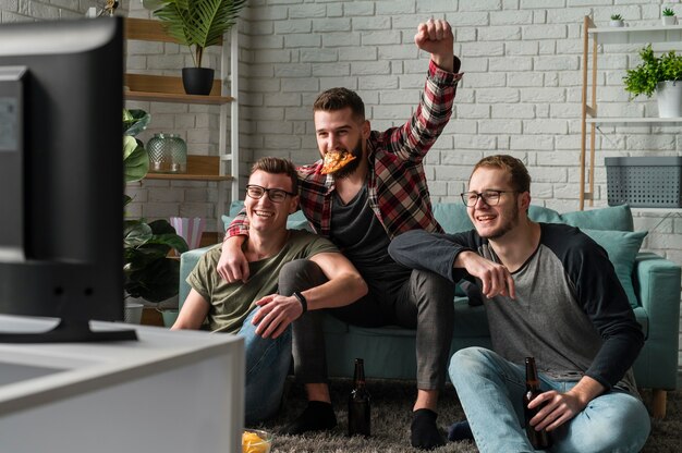 Vista frontal de amigos do sexo masculino comendo pizza e assistindo esportes na tv