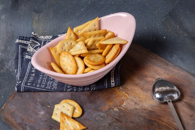 Vista frontal de batatas fritas e bolachas no interior da chapa branca na mesa de madeira e superfície cinza