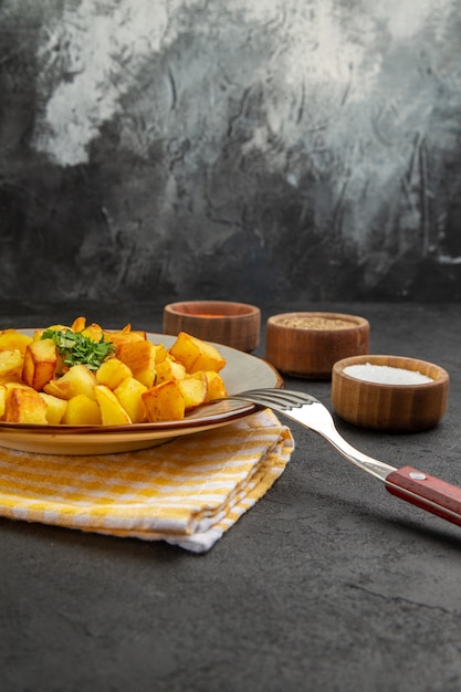 Vista frontal de batatas fritas saborosas dentro do prato com temperos em uma mesa escura