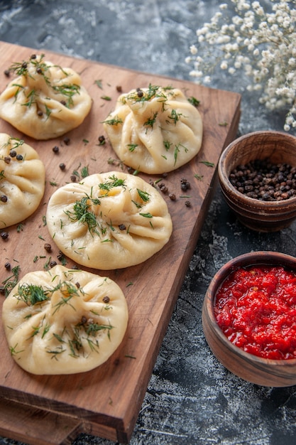 Vista frontal de bolinhos de massa crus com molho de tomate e temperos em uma superfície cinzenta massa de carne refeição bolo cozinhando prato cozinha jantar