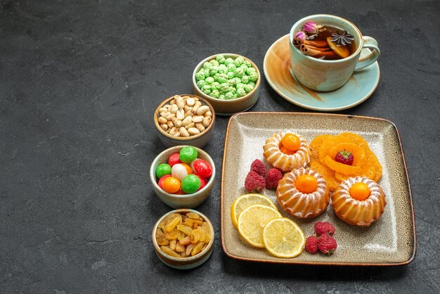 Vista frontal de bolinhos deliciosos com doces, frutas e nozes no espaço cinza