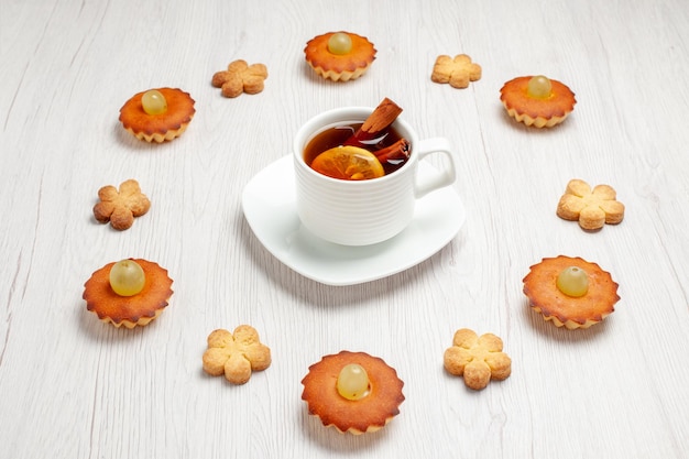 Vista frontal de bolinhos deliciosos forrados com biscoitos e xícara de chá no chão branco