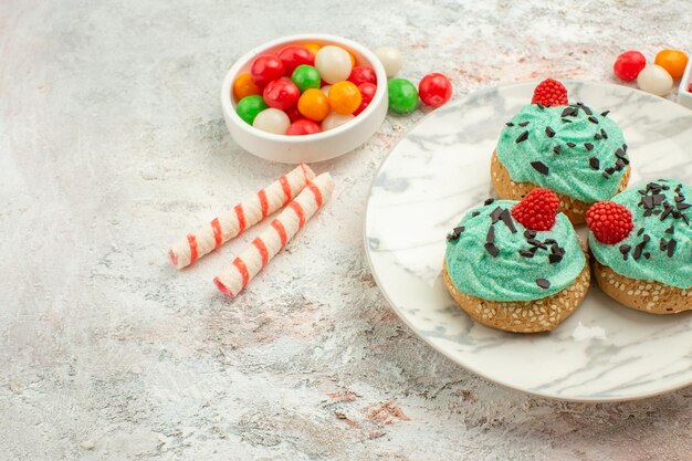 Vista frontal de bolos deliciosos de creme com doces coloridos em fundo branco bolo biscoito doce sobremesa creme