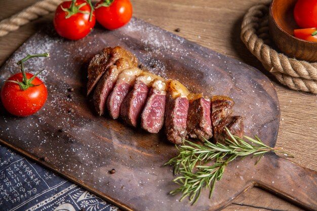 Vista frontal de carne fatiada frita com verduras e tomates vermelhos frescos na mesa de madeira