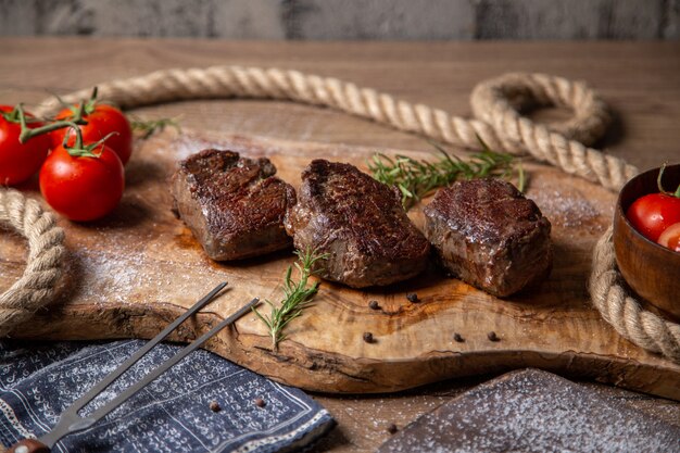 Vista frontal de carne saborosa frita com tomates vermelhos frescos e verduras na mesa de madeira