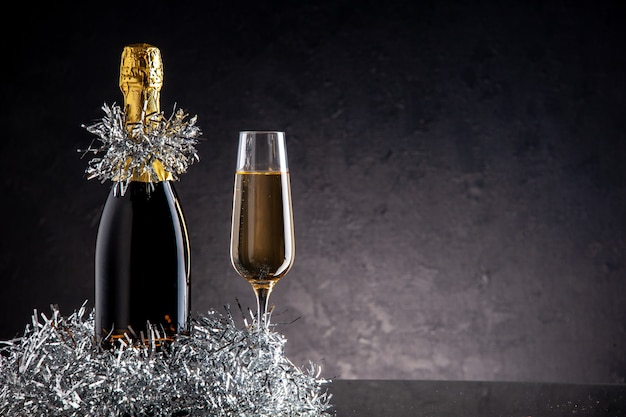 Vista frontal de champanhe em garrafa e copo em superfície escura