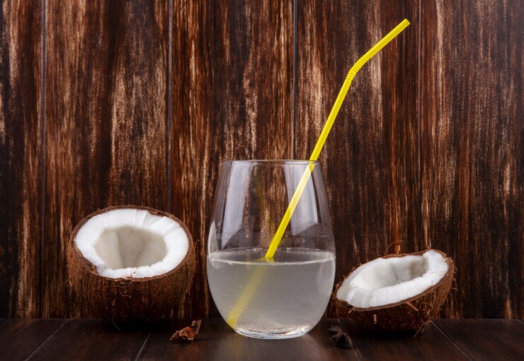 Foto grátis vista frontal de cocos cortados ao meio e frescos com um copo de água sobre uma superfície de madeira