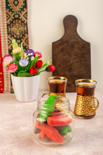 Vista frontal de coloridos deliciosos biscoitos diferentes formados dentro da lata com flores e xícaras de chá