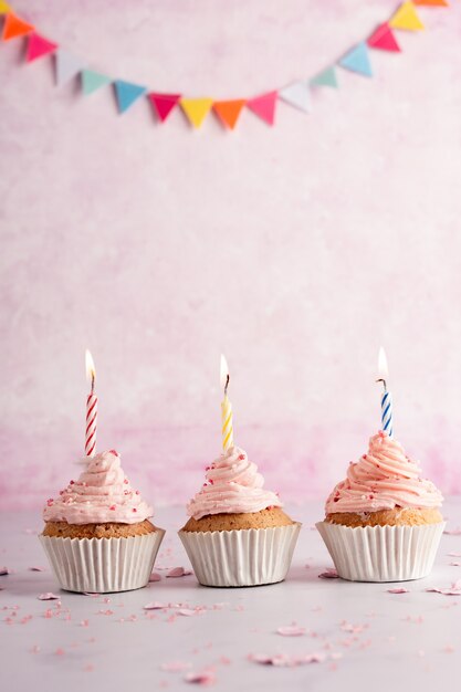 Vista frontal de cupcakes de aniversário com guirlanda e velas acesas