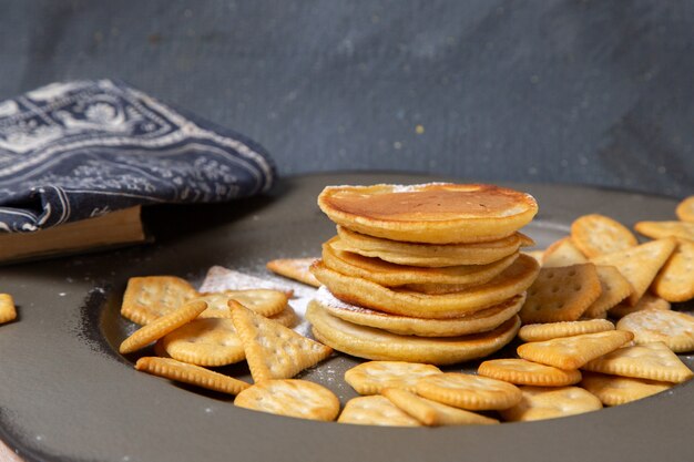 Vista frontal de deliciosas panquecas com biscoitos na superfície cinza