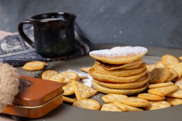 Vista frontal de deliciosas panquecas com copo preto de leite na superfície cinza