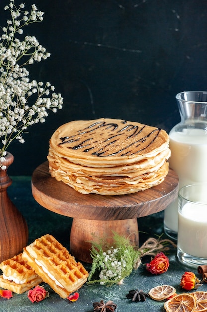 Vista frontal de deliciosas panquecas com leite em uma superfície azul-escura