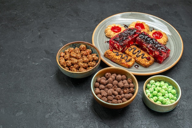 Vista frontal de deliciosos bolos de frutas com biscoitos e doces no espaço escuro