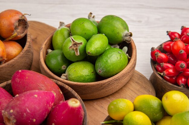 Vista frontal de diferentes frutas feijoas bagas e outras frutas dentro de pratos na mesa branca comida madura exótica foto colorida