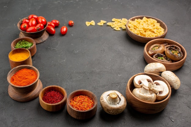 Vista frontal de diferentes temperos com tomates e cogumelos na mesa escura de pimenta picante