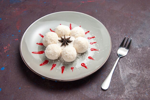 Vista frontal de doces deliciosos de coco redondo formado com glacê vermelho no espaço escuro