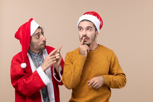 Vista frontal de dois amigos com chapéu de Papai Noel pensando em fundo bege isolado