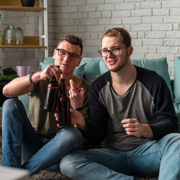 Vista frontal de dois amigos do sexo masculino assistindo esportes na tv e tomando cerveja