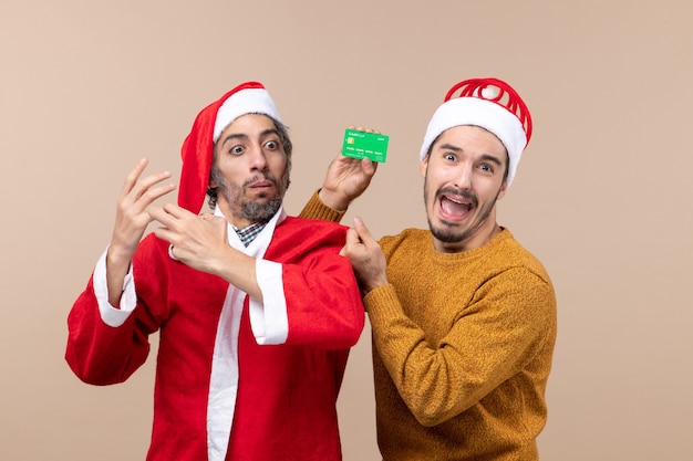 Vista frontal de dois caras, um com um casaco de Papai Noel e o outro com um cartão de crédito confuso em um fundo bege isolado