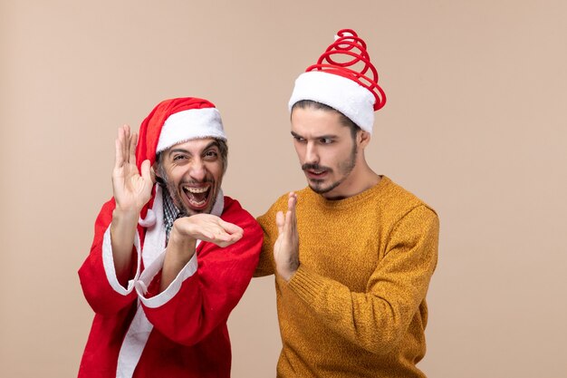 Vista frontal de dois homens com chapéu de Papai Noel batendo palmas em um fundo bege isolado