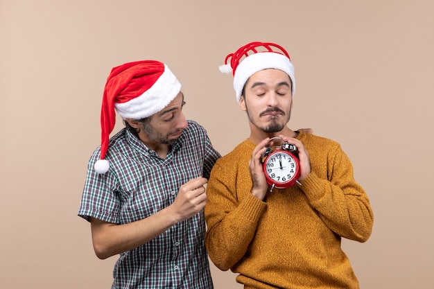 Vista frontal de dois homens de natal, um segurando um despertador com as duas mãos em um fundo bege isolado