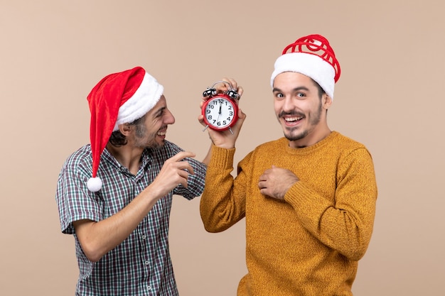 Vista frontal de dois homens felizes, um segurando um despertador e o outro desligando-o em um fundo bege isolado