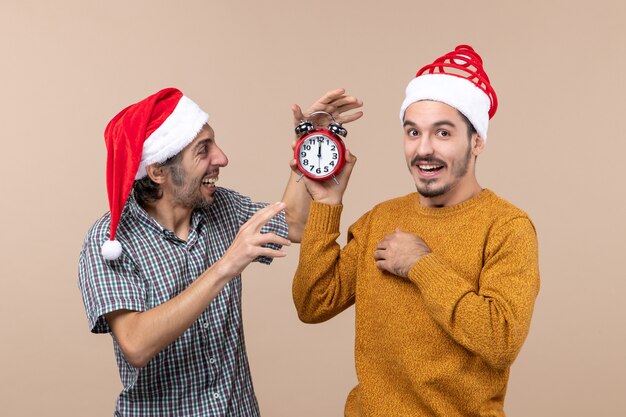 Vista frontal de dois homens, um segurando um despertador e o outro desligando-o em um fundo bege isolado