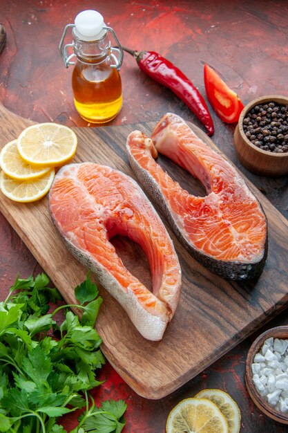 Vista frontal de fatias de peixe cru com verduras e limão em um prato de comida de cor escura.