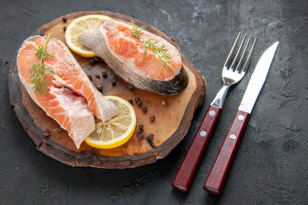Vista frontal de fatias de peixe fresco com limão e talheres em um prato escuro com fotos de carnes e frutos do mar