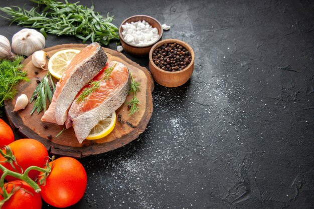 Vista frontal de fatias de peixe fresco com tomate e fatias de limão em um prato de frutos do mar de cor escura com comida crua