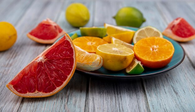 Vista frontal de fatias de toranja com limão e laranja em um prato sobre fundo cinza