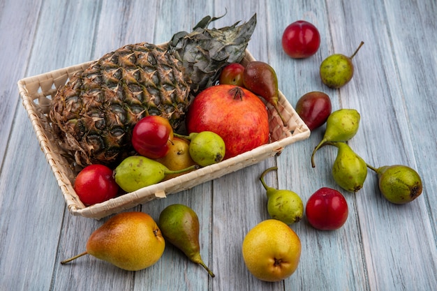 Foto grátis vista frontal de frutas como abacaxi romã ameixa pêssego na cesta e na superfície de madeira