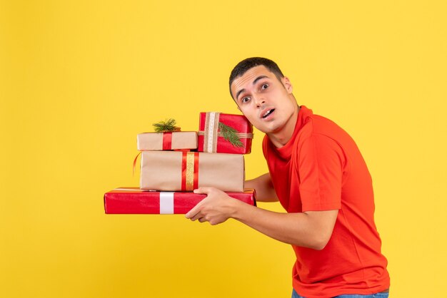 Vista frontal de jovem segurando presentes de Natal na parede amarela